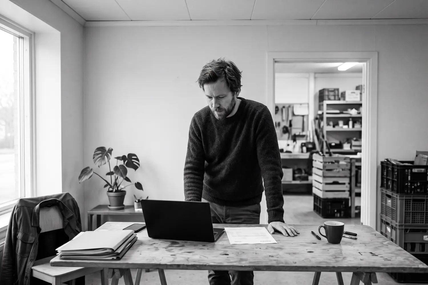 Inkassobolag för företag – företagare granskar en obetald faktura vid laptopen i sitt verkstadskontor, Agera Pay
